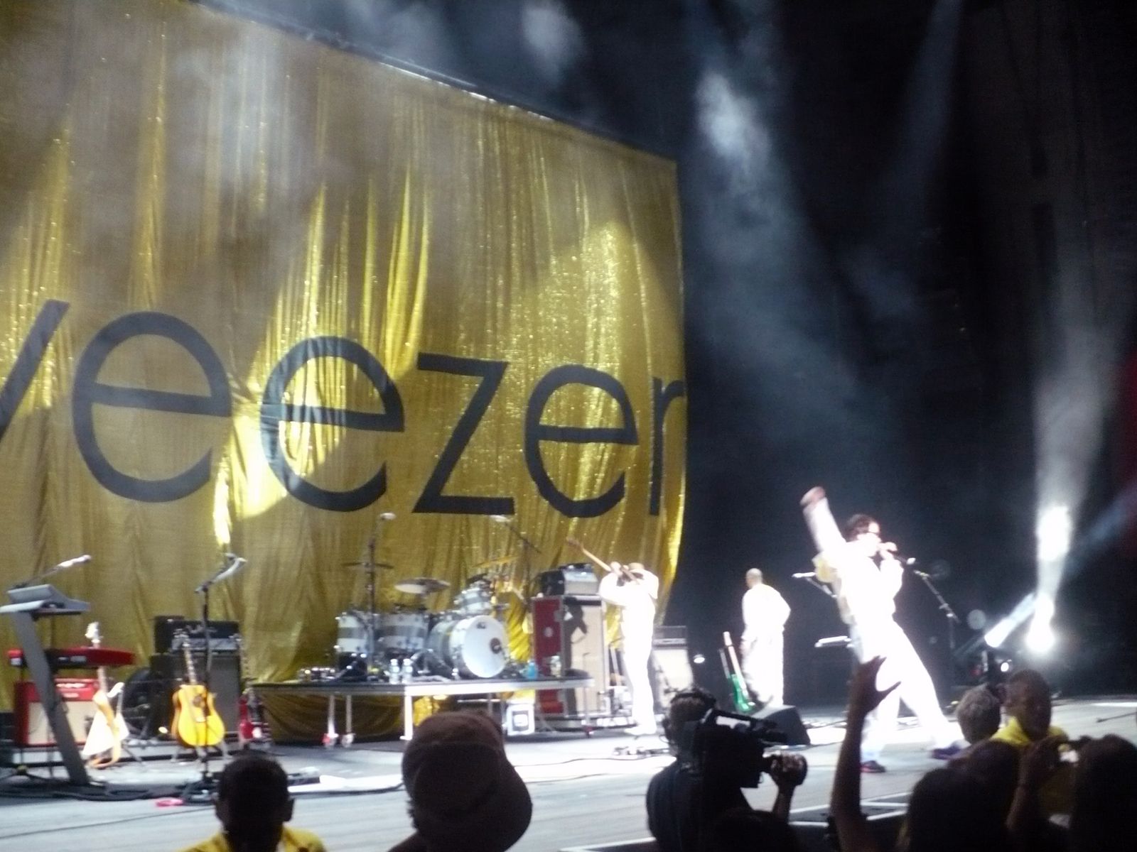 Weezer performing in front of a massive gold sequined backdrop with the band name on it, all members in white