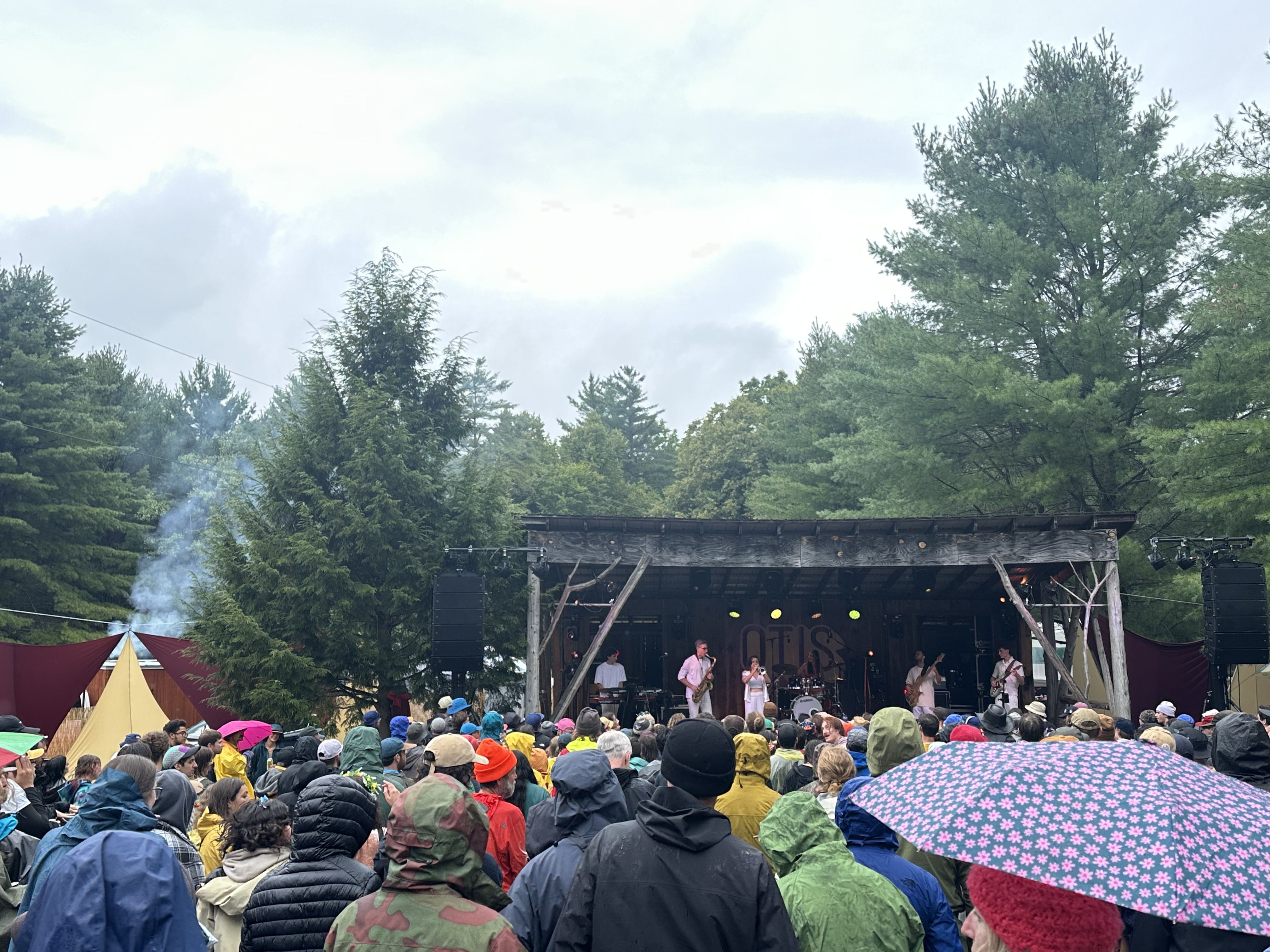 A band playing all in white clothing, some horns, some rock instruments, in a rustic woods setting