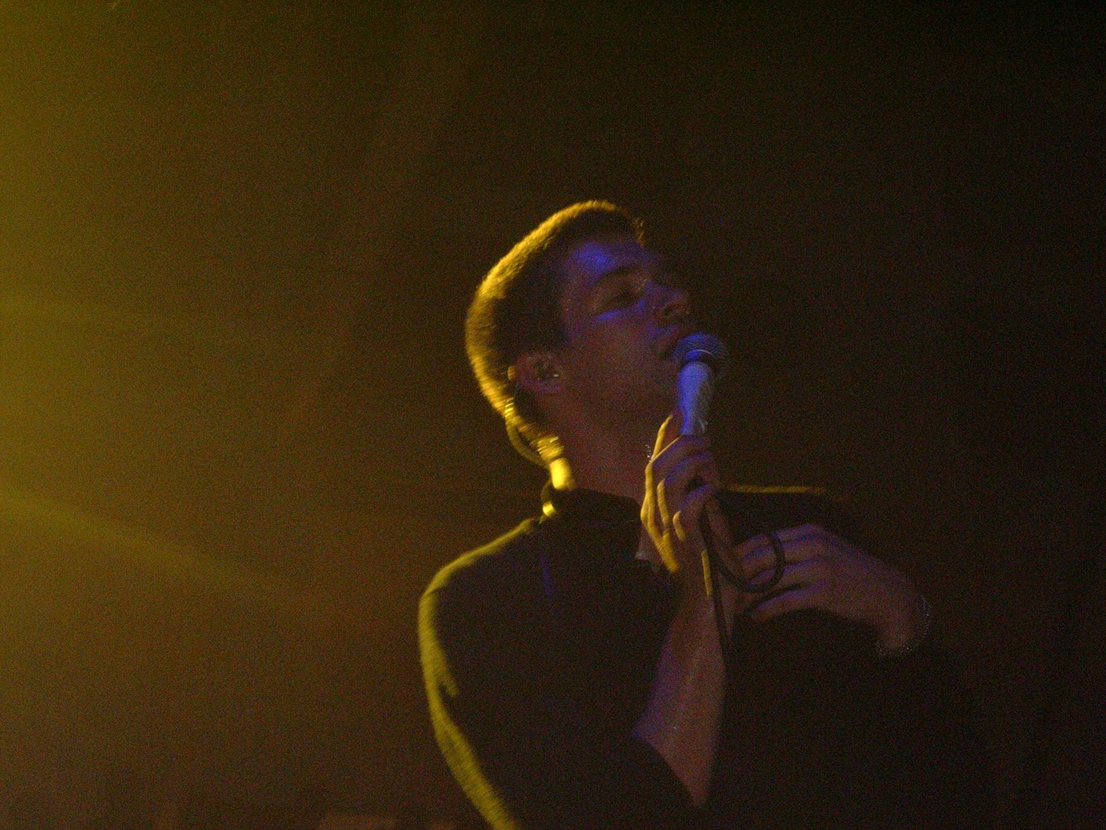 Adam Lazzara of Taking Back Sunday singing with mic in hand, lit in gold and blue stage light