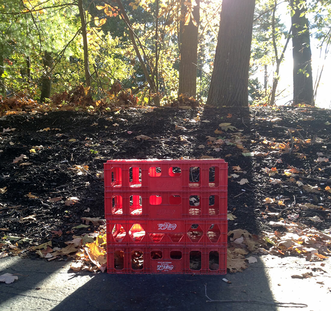 A red coca cola plastic bin on the edge of a parking lot