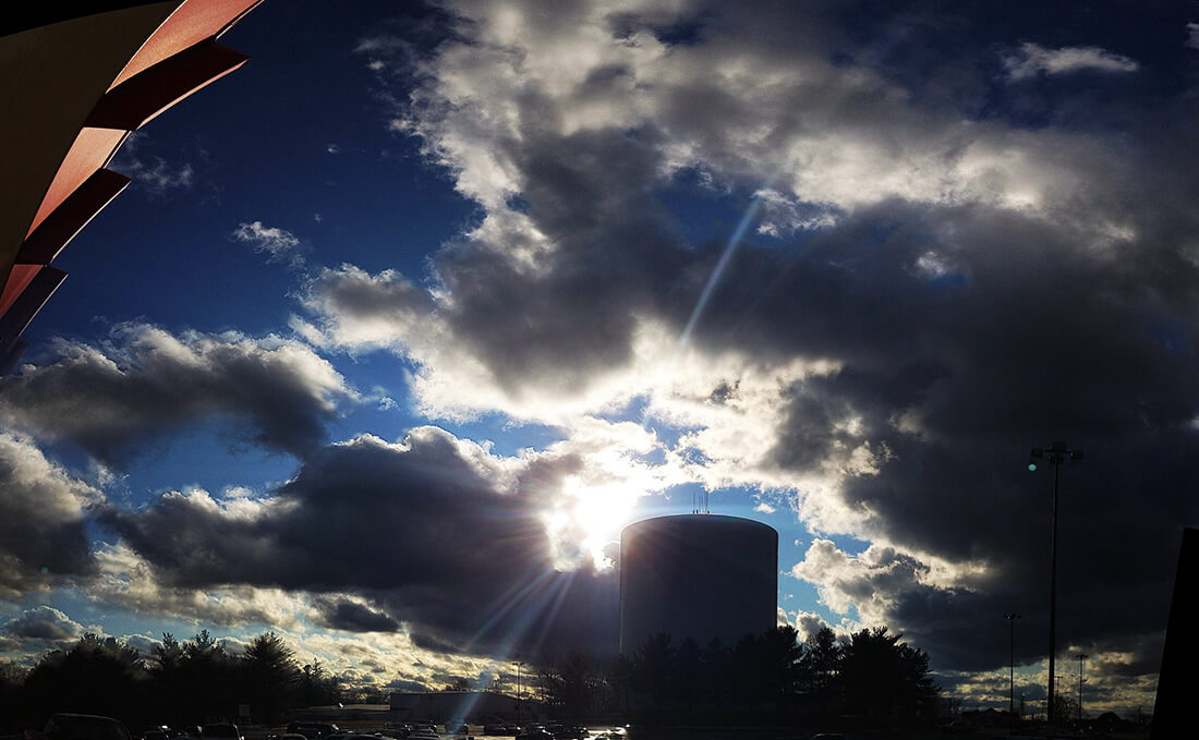  photograph looking into the sun of a fish eye panorama where the town water tower and clouds is blocking the sun