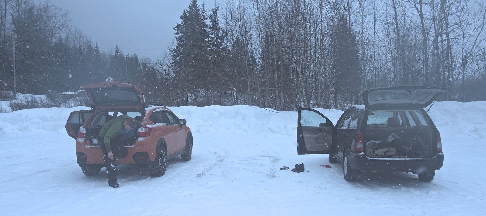 hiker taking off their microspikes at the trailhead parking lot in snowy, gray