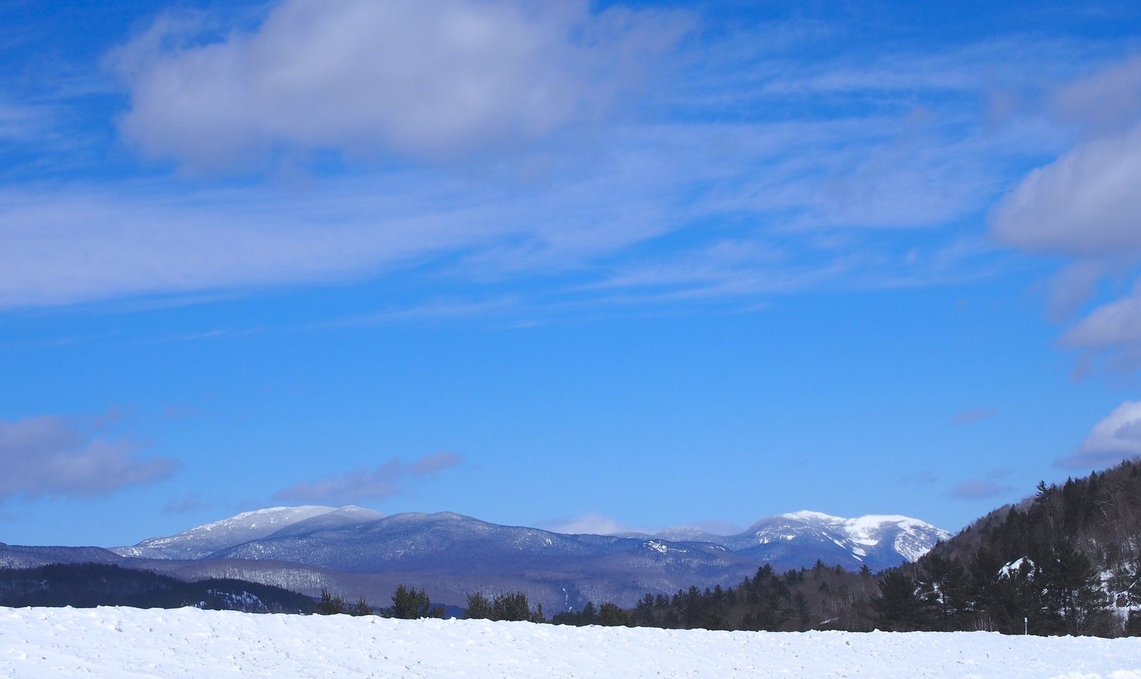 snow in the foreground, snow-capped mountains in the mid-ground, and a big beautiful blue sky in the background.