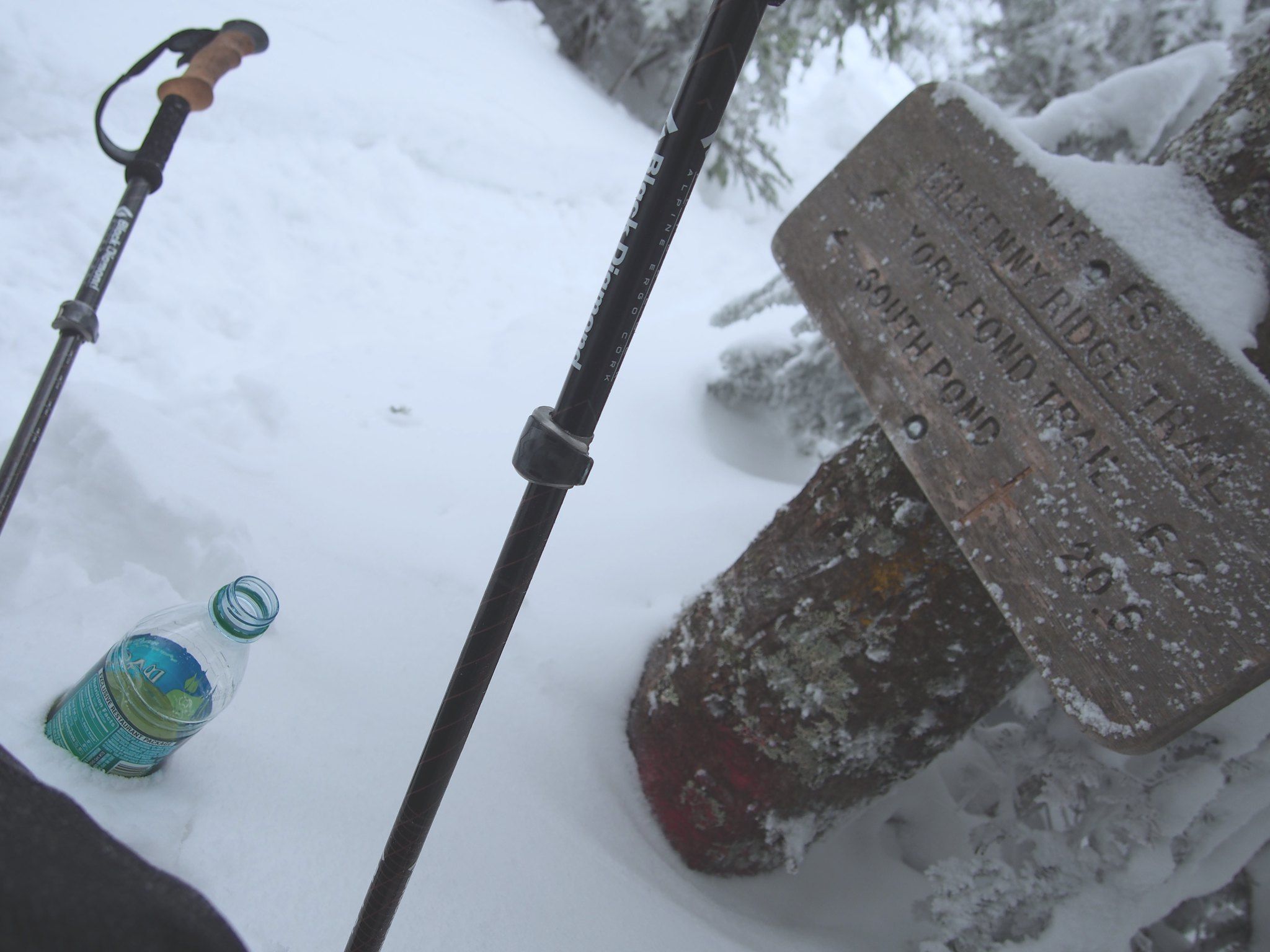 Waterbottle filled with a celebratory liqeur, trail sign, and hiking poles on a snow covered ground